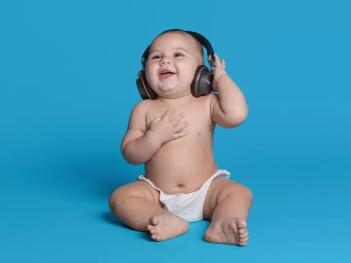 Un bébé souriant, en couche, écoute de la musique avec des écouteurs, le décibel maximum pour un bébé est à éviter.