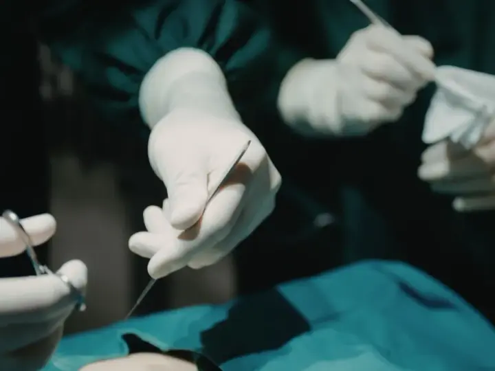 Dłonie chirurga w rękawiczkach trzymające narzędzia chirurgiczne i gazę podczas operacji.