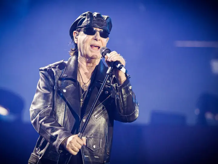 Klaus Meine, jung und rockig, singt ins Mikrofon, trägt Lederjacke und Kappe.