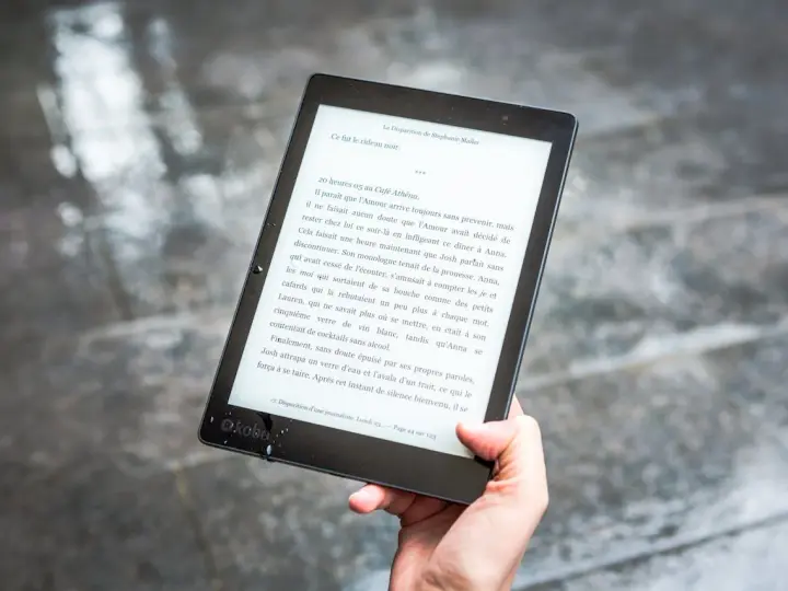 Ręka trzyma czytnik ebooków z tekstem. Czytanie książek elektronicznych to przyjemność, a teraz dzięki zmianom w prawie, vat na ebooki jest korzystniejszy.