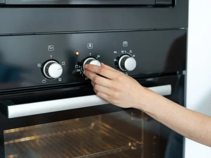 Hand dreht Temperaturregler am Ofen auf 250 Grad. Die Frage "wie lange Ofen vorheizen" wird durch das Einstellen der Temperatur beantwortet.