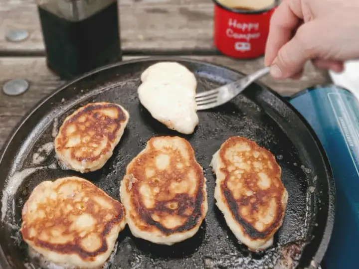 Frying pancakes in a cast iron skillet is a delicious answer to what to eat when camping. A fork lifts a fresh pancake, ready for syrup.