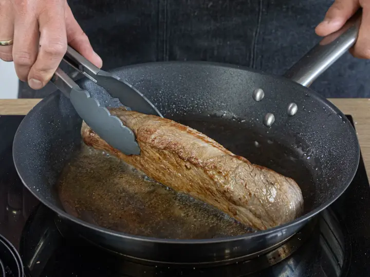 Ein saftiges Schweinefilet brät in der Pfanne. Einfache Rezepte für zartes Fleisch in der Pfanne gelingen so.