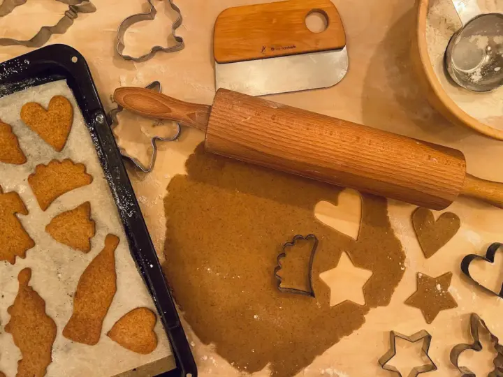 Pepparkaksdeg recept förbereds med kavel och pepparkaksformar. Färdiga pepparkakor ligger på en plåt.