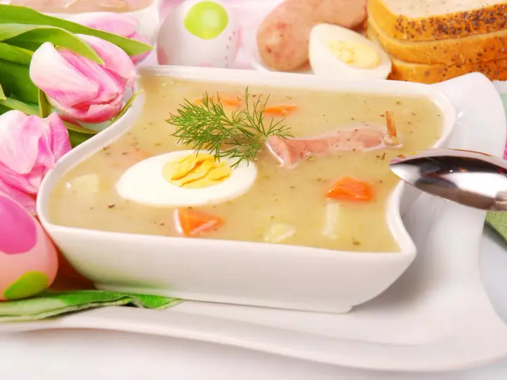 Biały barszcz z jajkiem, kiełbasą, marchewką i koprem, ozdobiony tulipanami i pisankami.