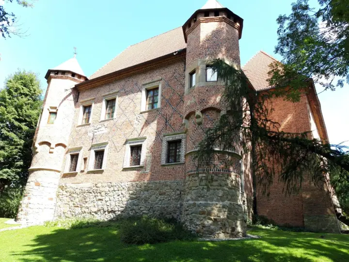 Zamek w Dębnie Polskim, ceglana budowla z kamiennym cokołem, otoczona zielenią.