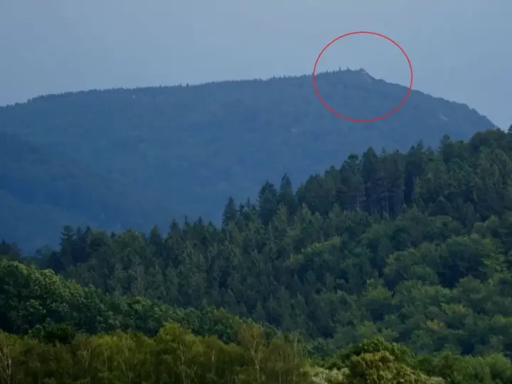 Górzyste krajobrazy czeskich Izery, z zalesionymi zboczami i skalistym szczytem zaznaczonym czerwoną obwódką.