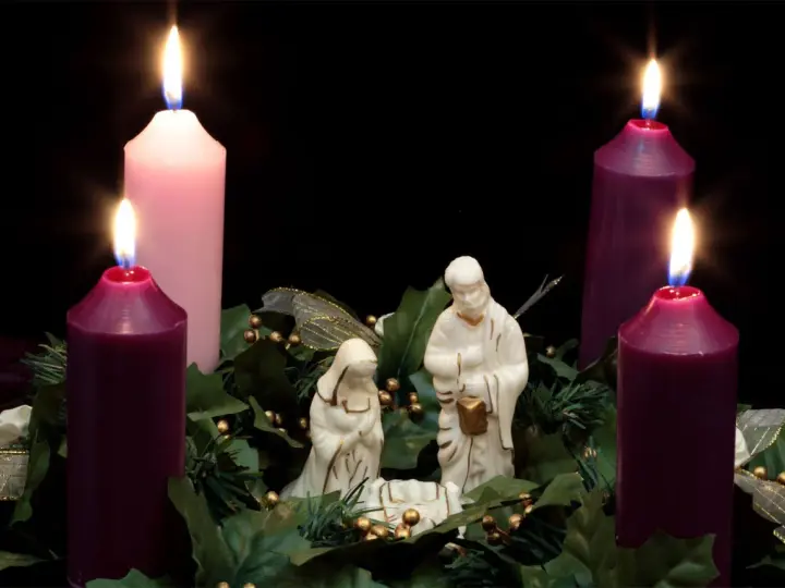 Three lit candles, two purple and one pink, surround a nativity scene. This is the advent 3rd Sunday.