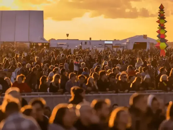 Tłum ludzi na festiwalu, zachód słońca. Kolorowa instalacja artystyczna w tle. Kto będzie następny na scenie?