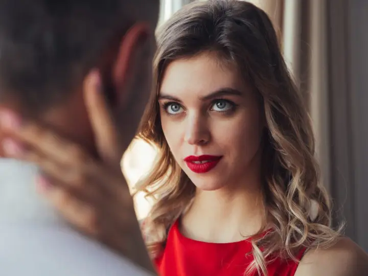 Un homme regarde intensément une femme aux yeux bleus et aux lèvres rouges, vêtue d'une robe rouge.