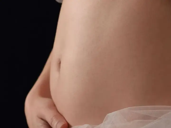 Pancia gonfia e dura, sembro incinta. La pelle liscia e chiara, con un leggero velo di tessuto rosa chiaro.