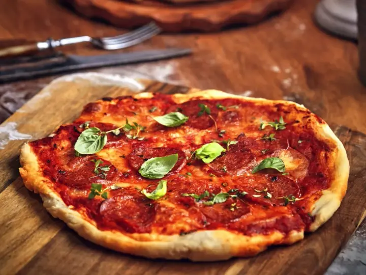 Pikantna spianata calabrese na pizzy, ozdobiona świeżą bazylią i ziołami, czeka na talerzu.