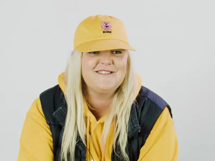 Frau mit gelber Kappe und Kapuzenpullover lächelt.