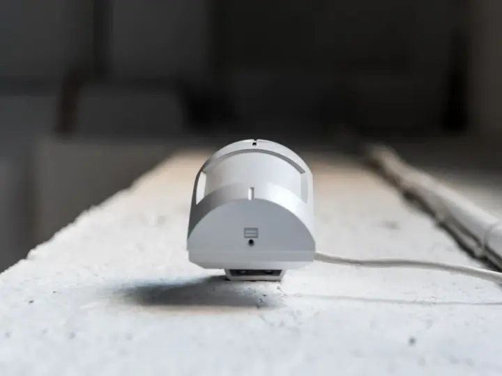 Detector de presencia y movimiento blanco, con cable, montado en superficie rugosa.