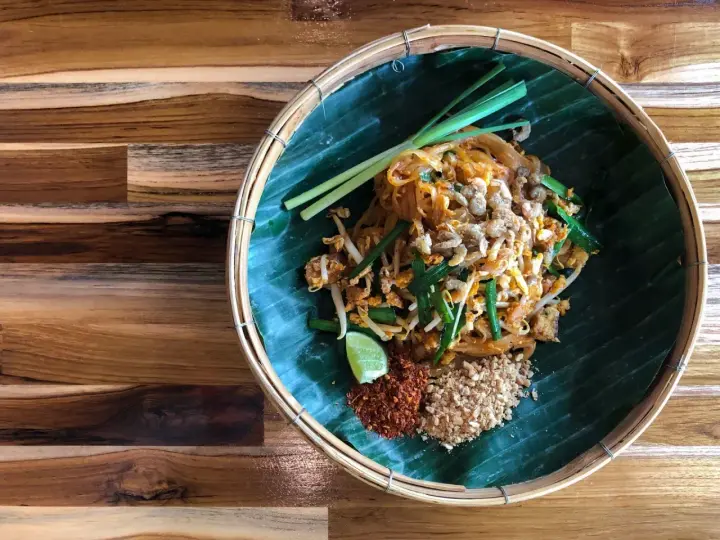 Pyszne pad thai skladniki: makaron ryżowy, kiełki, szczypiorek, orzeszki ziemne, chili i limonka na liściu bananowca.