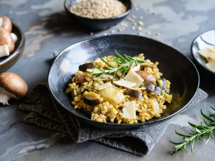 Miseczka risotto z grzybami i parmezanem, udekorowana rozmarynem.