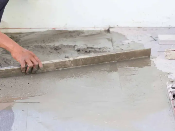 Ręka wyrównuje świeży beton, tworząc idealnie gładką podłogę na gruncie.