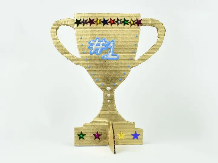 Trofeo de cartón dorado, ideal para hacer trofeos personalizados. Luce un "#1" azul y estrellas de colores.