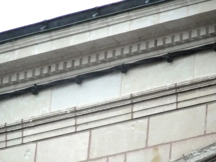 Détail d'une façade en tuffeau avec des câbles noirs fixés. L'image montre comment poncer du tuffeau pour restaurer sa surface.