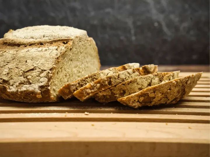 Ein rustikales, selbstgebackenes Brot liegt angeschnitten auf einem Holzbrett. Die Kruste ist knusprig, die Scheiben duften nach Tradition.