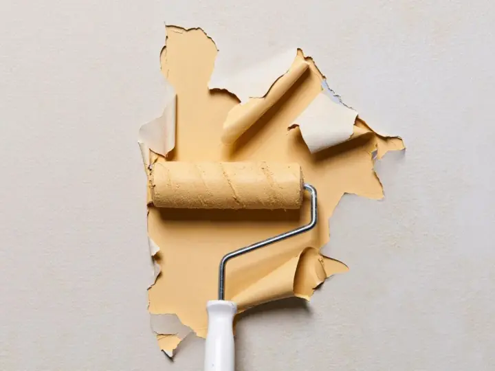 Un rouleau à peinture jaune révèle un mur où l'enduit ne tient pas, se décollant en lambeaux.