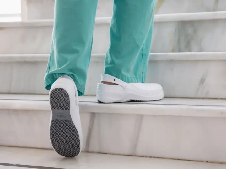 Persona subiendo escaleras con zapatos blancos, mostrando la suela antideslizante. El poliuretano en zapatos ofrece comodidad y durabilidad.