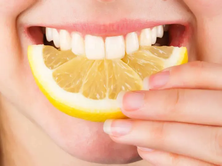 Une personne tient une tranche de citron près de sa bouche ouverte, révélant des dents blanches. Le citron est connu pour ses bienfaits sur la peau.