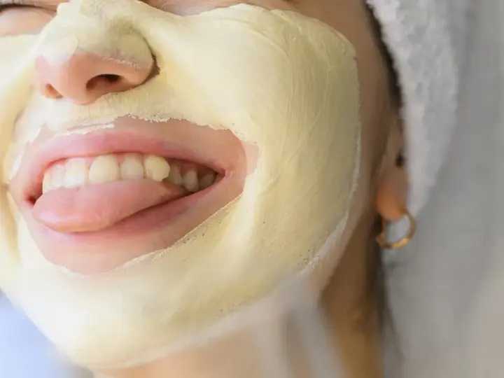 Una mujer se divierte con una mascarilla facial amarilla, sacando la lengua.