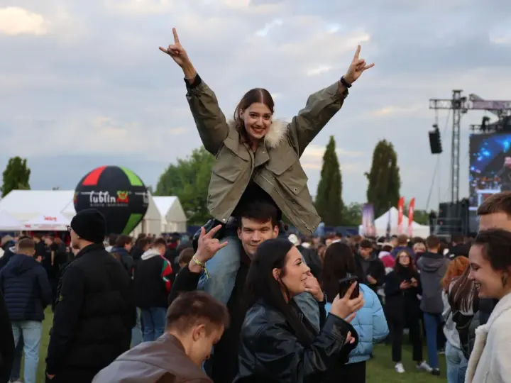 Dziewczyna na ramionach chłopaka cieszy się na Juwenaliach Politechniki Lubelskiej. W tle scena i tłum bawiących się studentów.