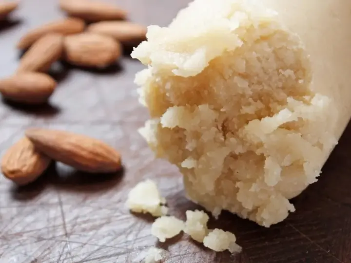 Frische Mandeln liegen neben einer Rolle Marzipan Rohmasse, bereit zum Verarbeiten.