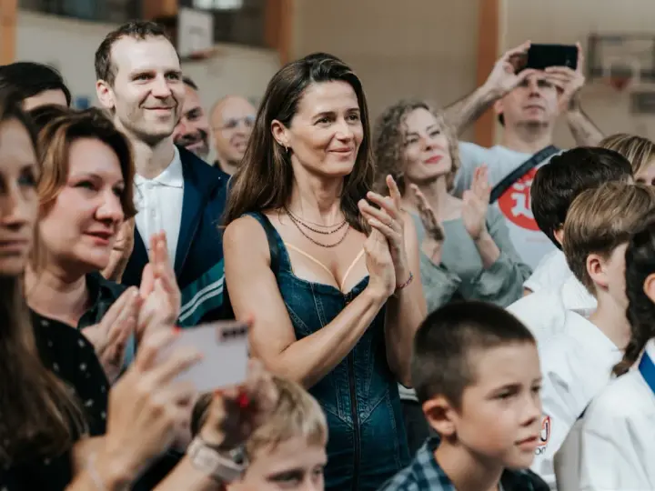 Agnieszka Grochowska z uśmiechem klaszcze, otoczona ludźmi na widowni.