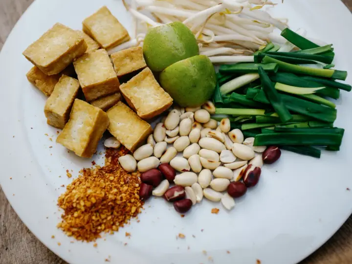 Talerz z pokrojonym tofu, orzeszkami ziemnymi, szczypiorkiem, kiełkami fasoli mung, limonkami i płatkami chili.