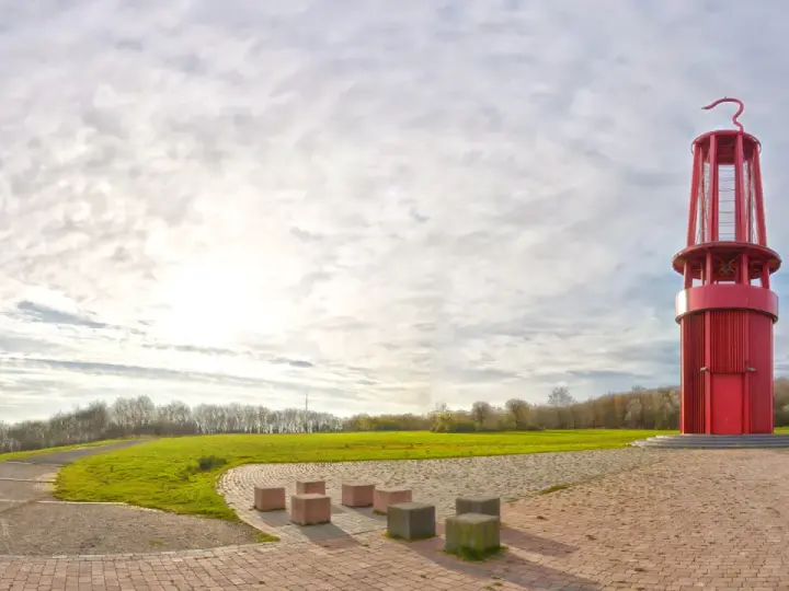 Rote Aussichtsturm auf der Halde Moers, umgeben von grünen Hügeln und einem weiten Himmel mit Wolken.