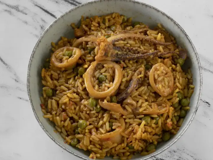 Un delicioso plato de arroz con calamares y guisantes, servido en un cuenco sobre una superficie de mármol.