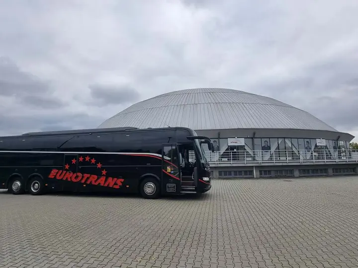 Czarny autokar firmy Eurotrans przed nowoczesnym budynkiem z kopułą.