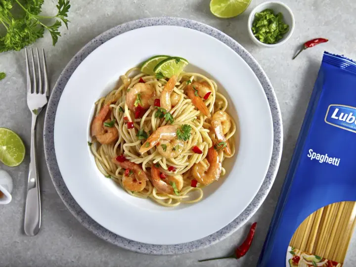 Pyszny makaron z krewetkami na winie, udekorowany limonką i natką pietruszki. Obok opakowanie makaronu spaghetti Lubella.