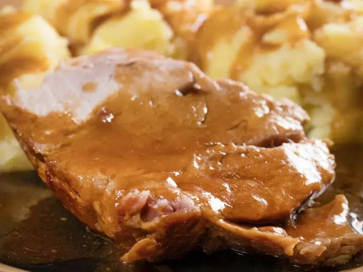 Mięciutka karkówka w sosie, podana z purée ziemniaczanym. Danie wygląda apetycznie i soczyście.