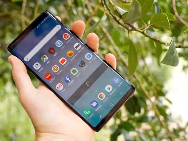 En hand håller en Samsung Galaxy Note 9 med många appar på skärmen, bland annat BankID och Spotify.