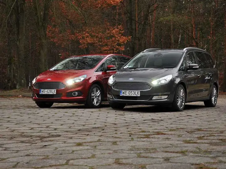 Dwa samochody Ford, czerwony S-Max i szary Galaxy, stoją na brukowanej nawierzchni w jesiennym lesie.