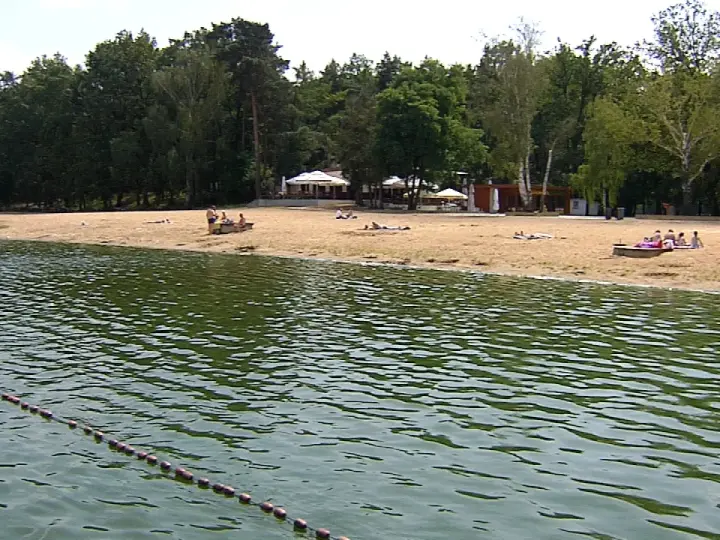 Plaża nad jeziorem Szperek, z kilkoma osobami odpoczywającymi na piasku i wodą w tle.
