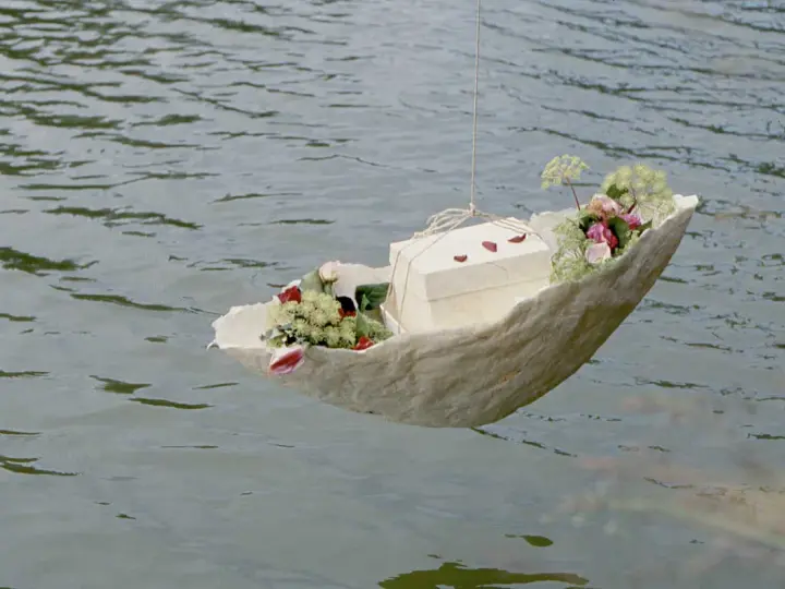 Ein Schiffchen mit Blumen und einer Schachtel schwimmt auf dem Wasser. Eine würdevolle Idee für Kinderbeerdigungen.
