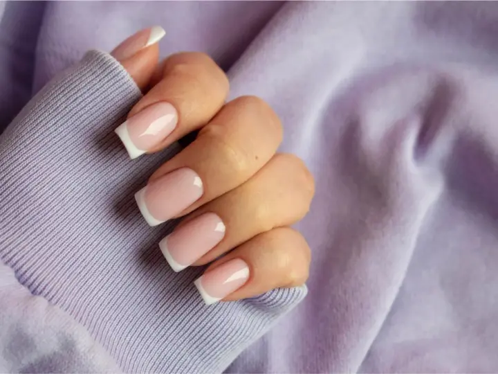 Dłoń z paznokciami w stylu french kolor, na tle lawendowej bluzy. Klasyka i elegancja.