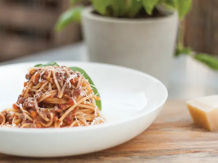 Pyszne spaghetti bolognese, przygotowane według oryginalnego przepisu, posypane parmezanem i udekorowane listkiem bazylii.