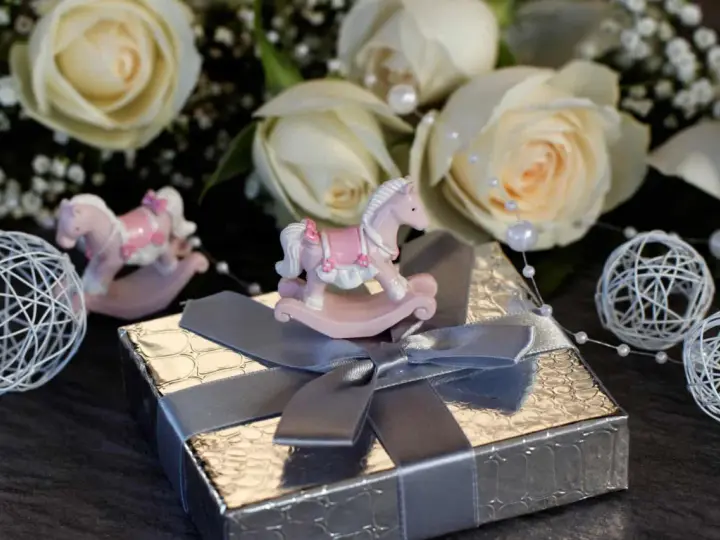 En rosa rosett baby-häst på en present. Bakgrunden är fylld med vita rosor och dekorationer.