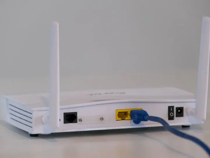Biały modem z dwiema antenkami, podłączony niebieskim kablem Ethernet. To urządzenie, które pozwala na połączenie z internetem.