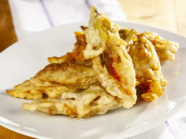 Fiori di zucca fritti dorati e croccanti su un piatto bianco, pronti per essere gustati.