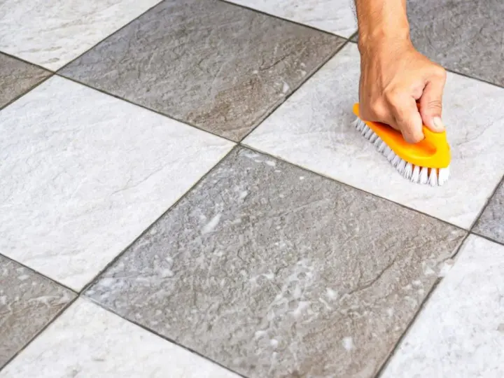 Main tenant utilise une brosse jaune pour faire briller le carrelage, révélant sa beauté naturelle.