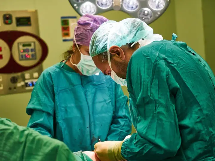 Chirurdzy w maseczkach i czepkach przygotowują się do operacji. Narkoza już działa, pacjent jest bezpieczny.