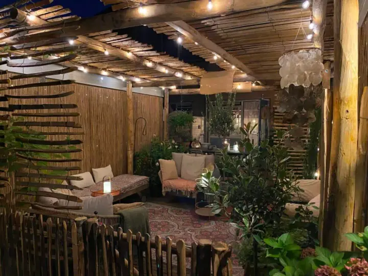 Une terrasse de jardin aménagée en coin cocooning, avec des banquettes confortables, des lumières douces et une ambiance chaleureuse.