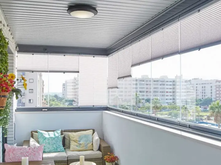 Ideas para tapar balcón: un espacio acogedor con sofá, plantas y vistas urbanas.